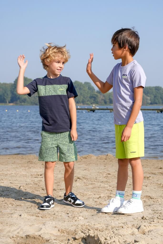 Two boys on a beach giving high fives with a body of water and trees in the background.