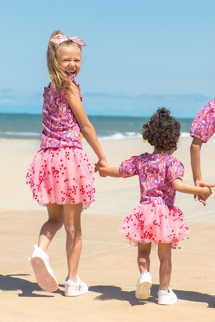 Three children in matching pink outfits on a beach with ocean in the background