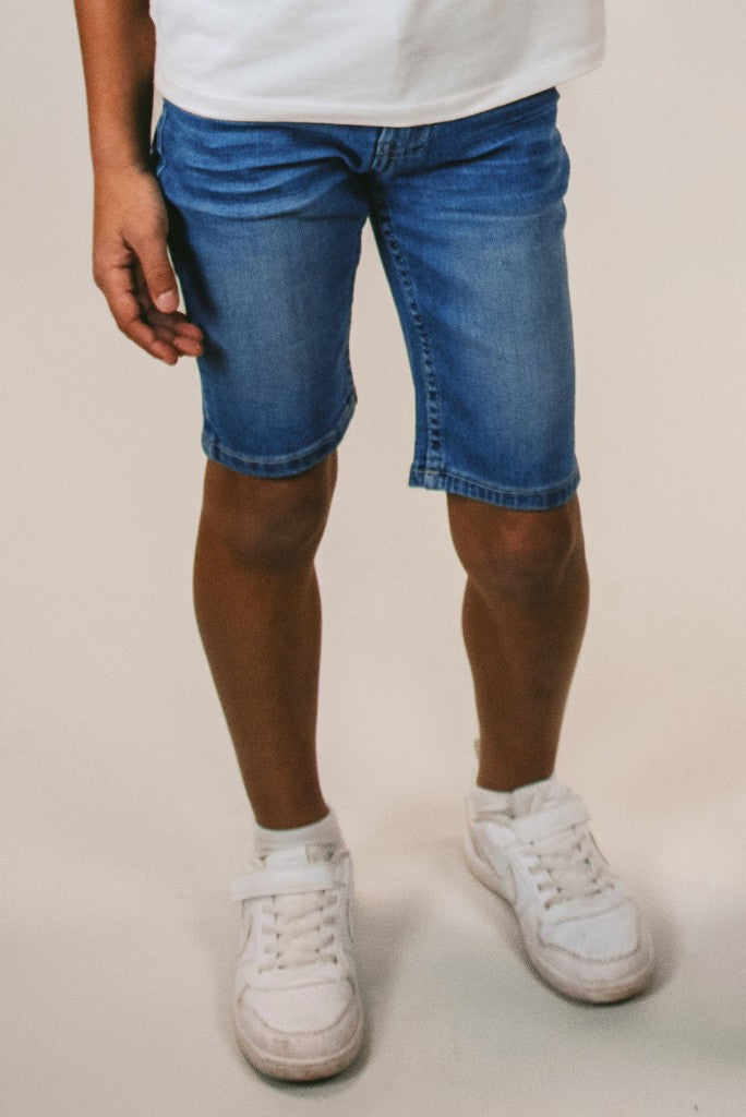 Boy wearing blue denim shorts 
Quinn and white sneakers on a plain background