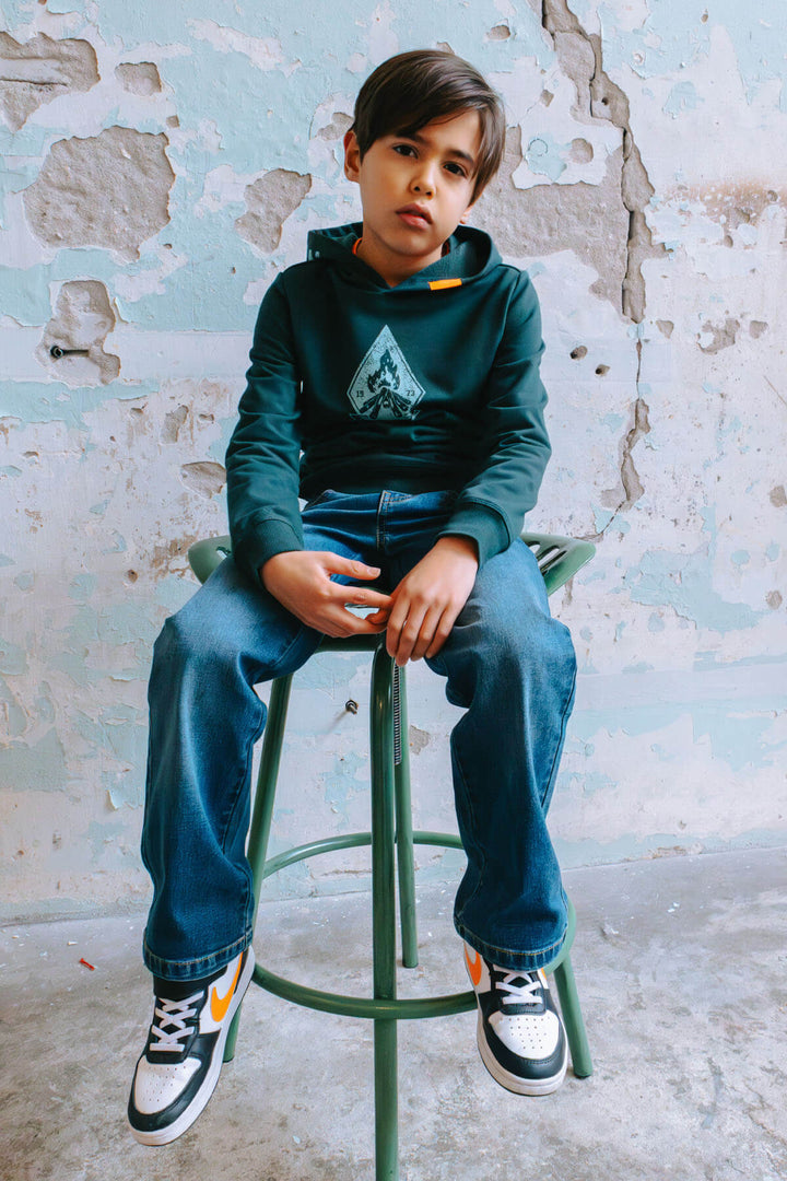 Boy sitting on a stool against a textured wall.