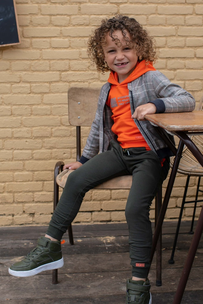 Side view of the boy sitting on a chair and wearing the Koert green track pants by Quapi