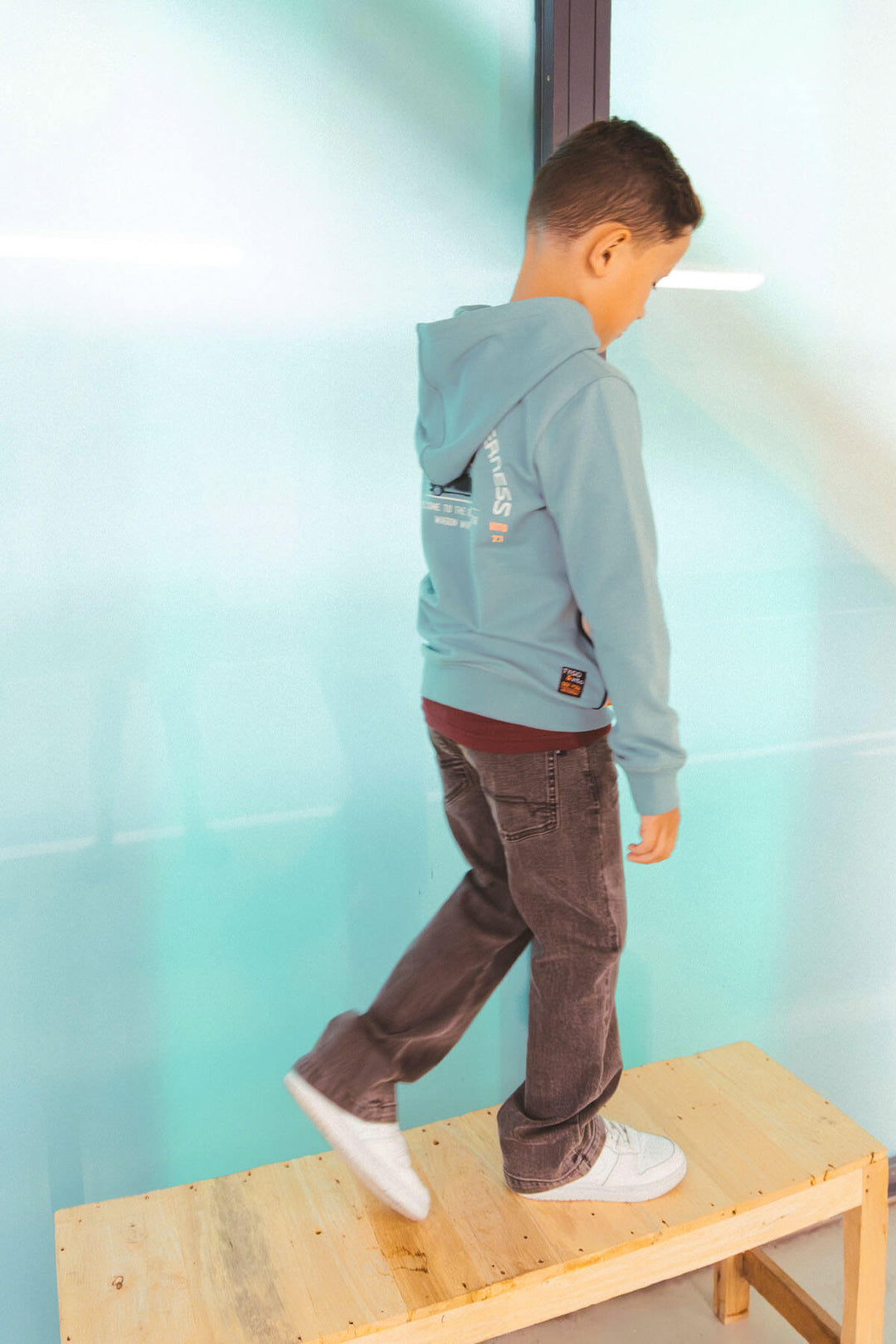 A boy standing with his back on the wooden platform wearing the loose fit jeans Loyd in grey