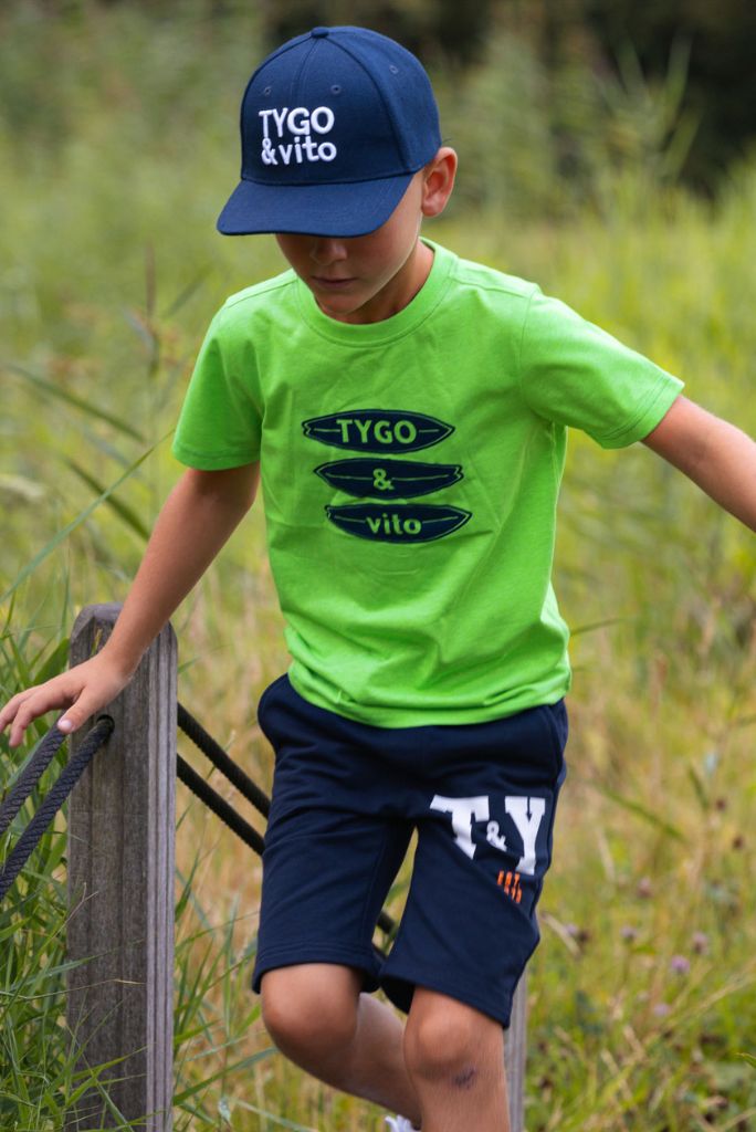 Boy wearing the green neon T-shirt James and navy shorts with visible branding in a natural setting