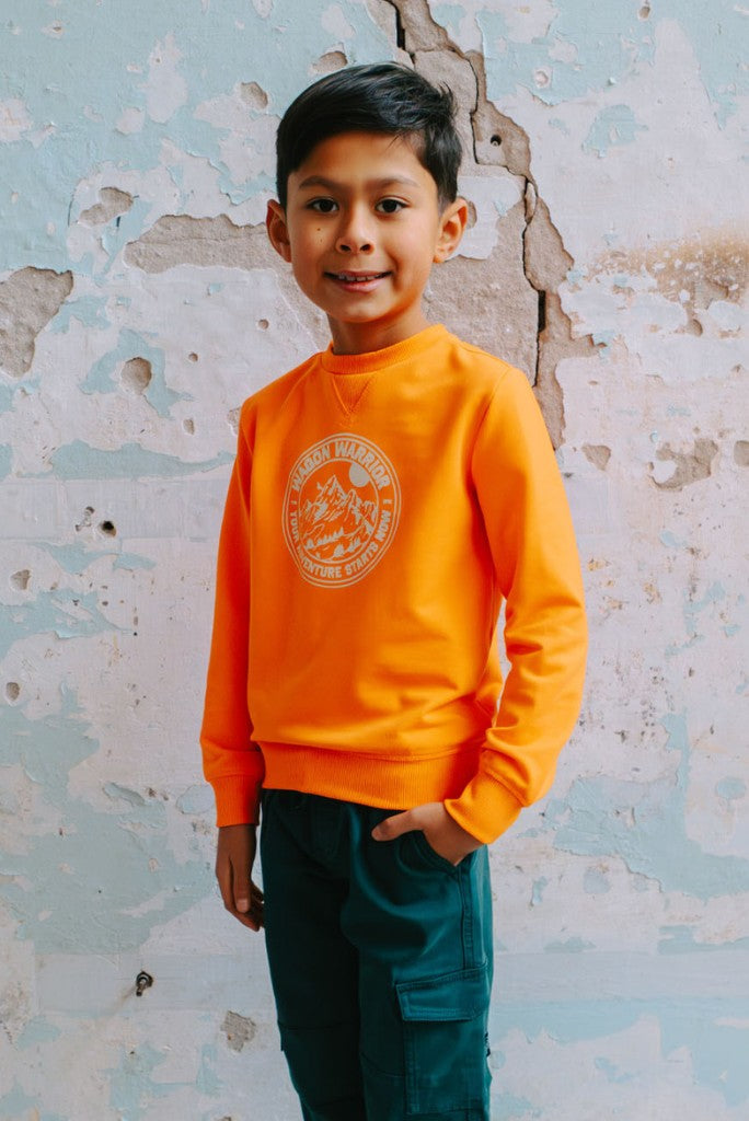 Boy wearing a neon orange sweatshirt with a logo against a textured wall.