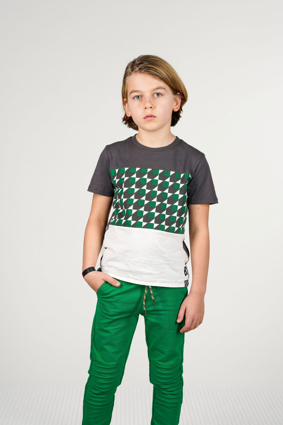 Boy wearing a gray t-shirt with a green and white pattern and green pants on a white background