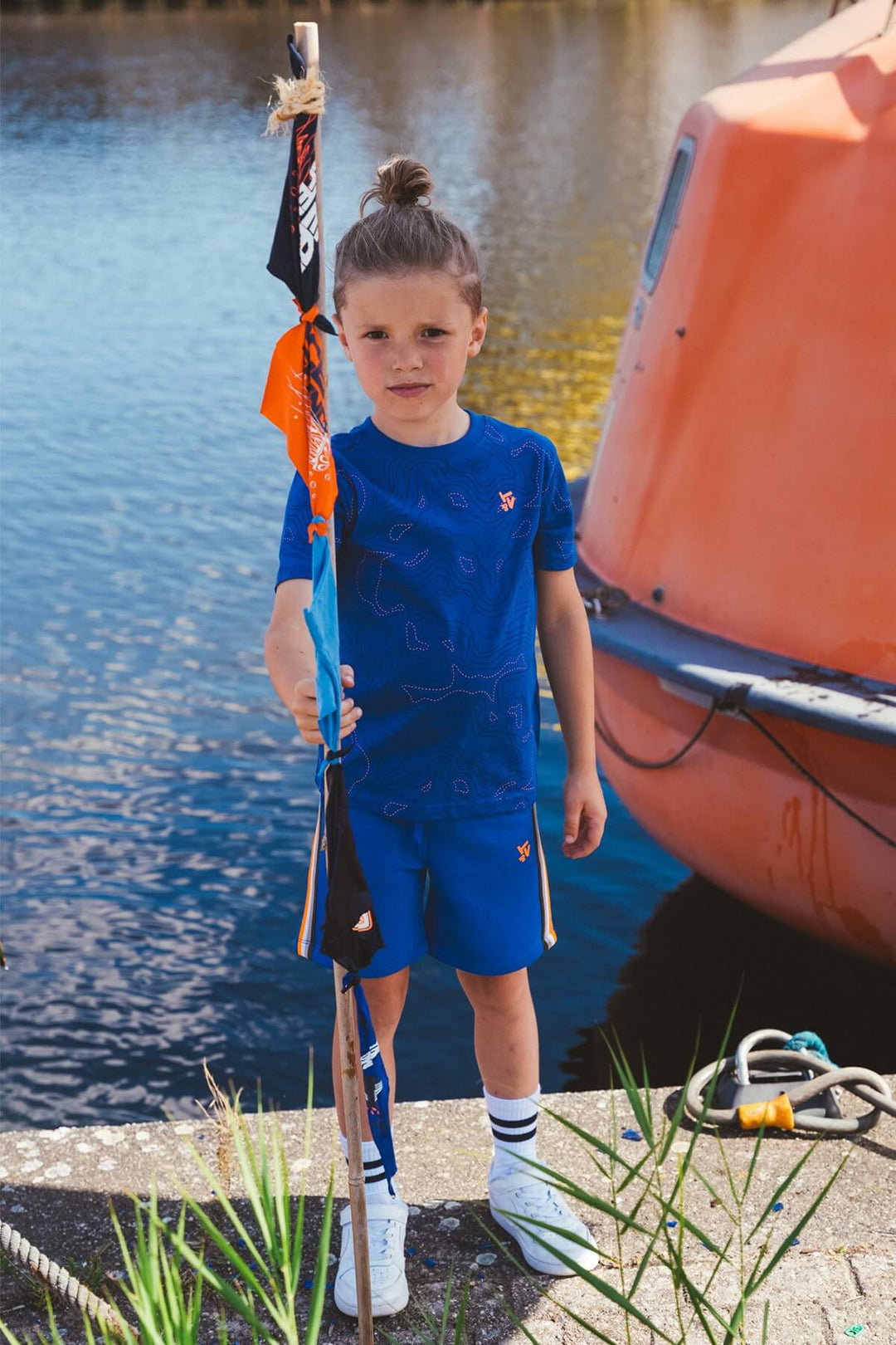 A Boy in blue outfit standing by a boat near water