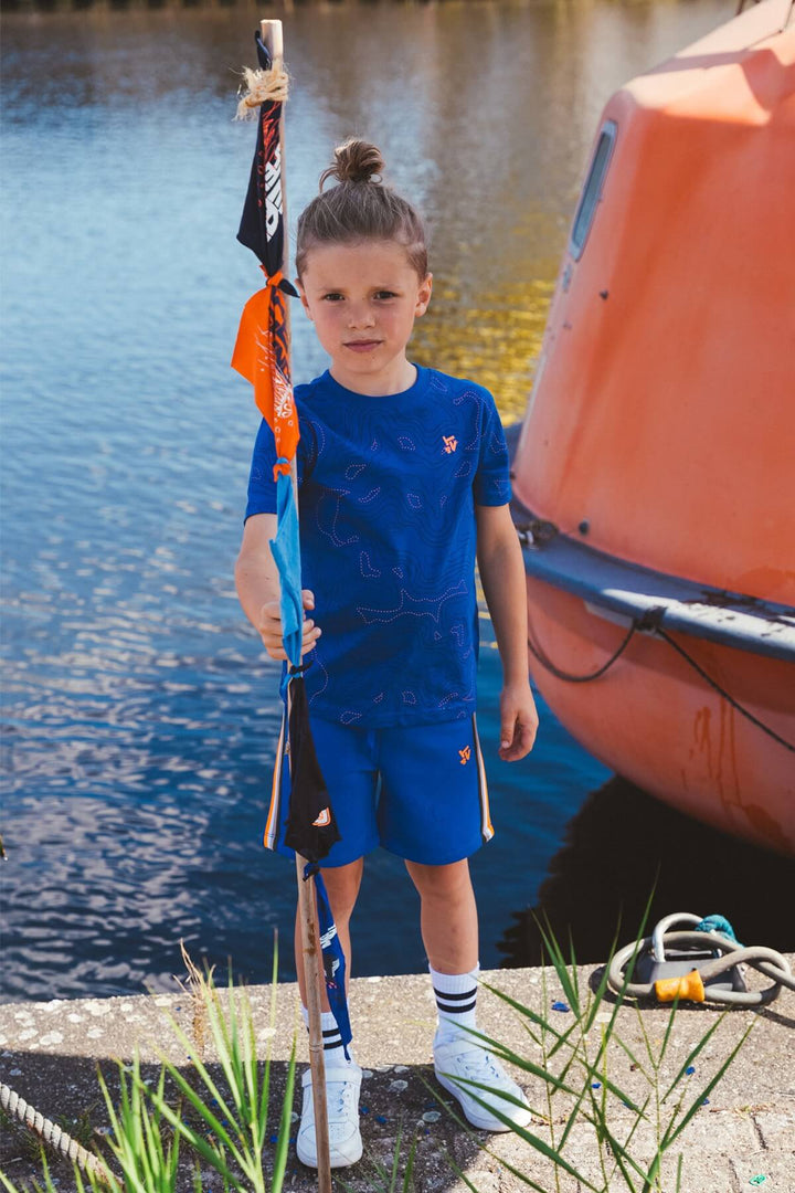 A Boy in blue outfit standing by a boat near water