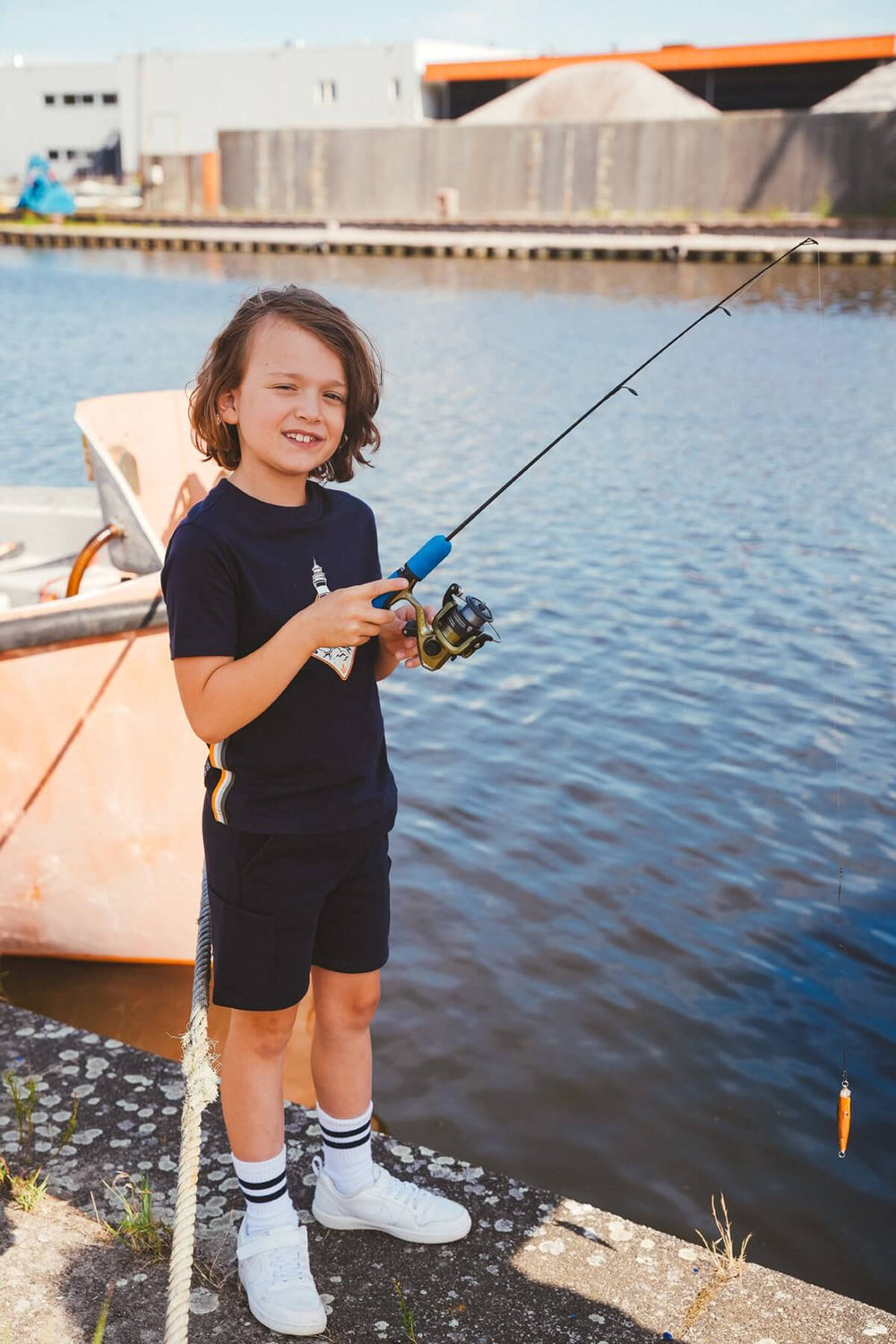 Boy fishing by a body of water with a boat in the background