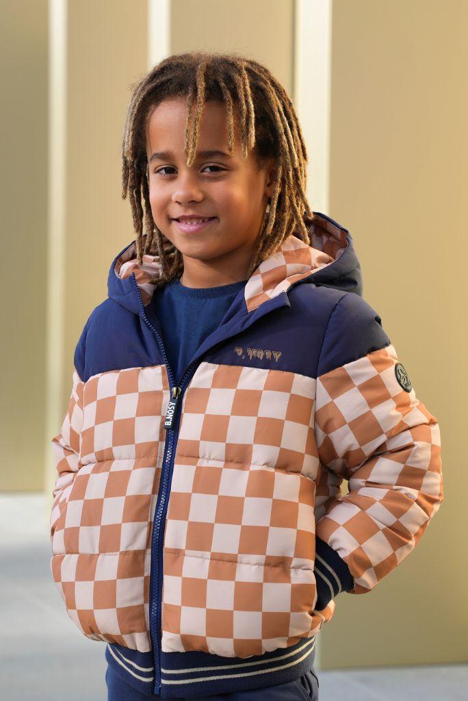 Boy wearing a checkered jacket with a visible brand logo, standing against a neutral background.