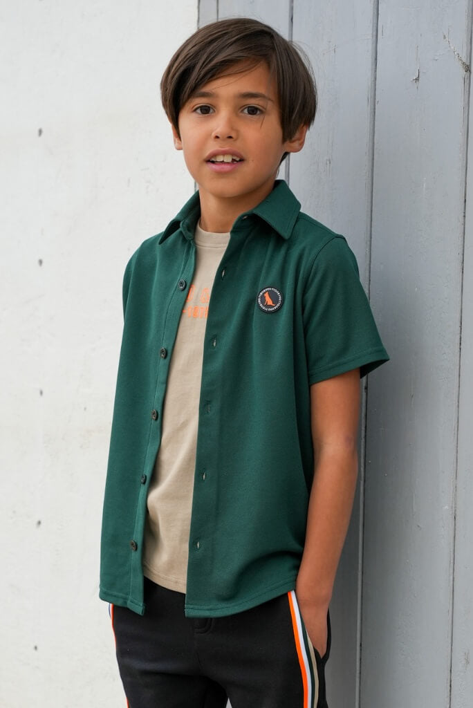 Young boy wearing a green shirt with a logo against a light gray wall