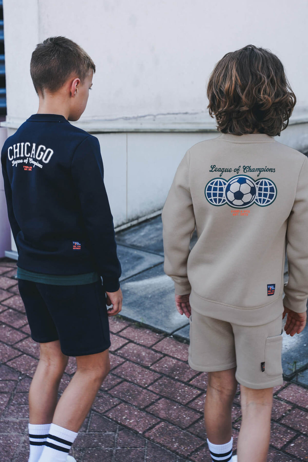 Two children wearing sweatshirts with visible branding on a sidewalk.