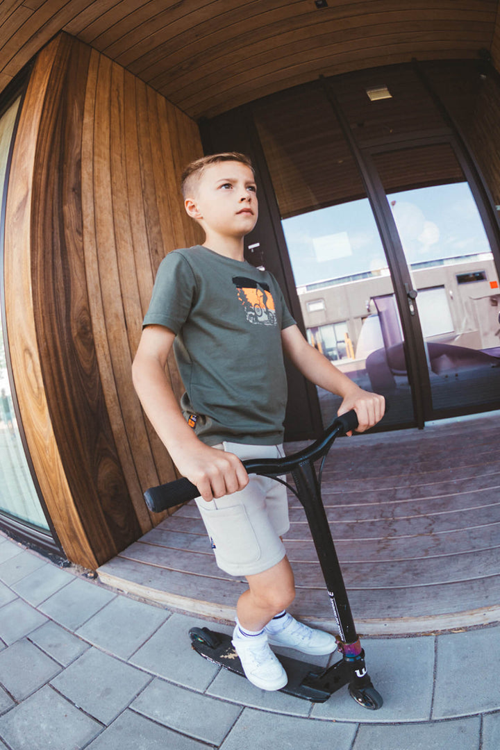 Young boy standing on a scooter in front of a modern building entrance.