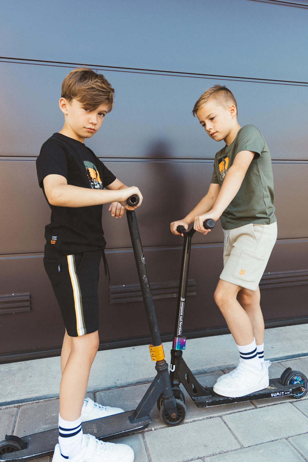 Two boys on scooters in front of a garage door