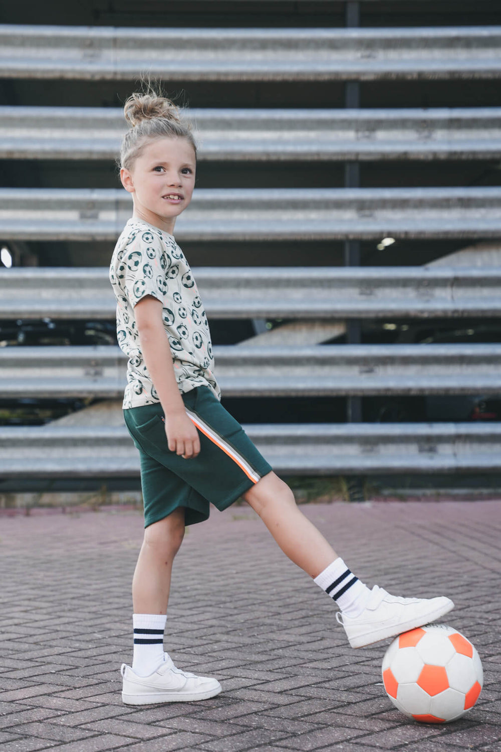 Boy playing with a soccer ball on a paved surface with bleachers in the background