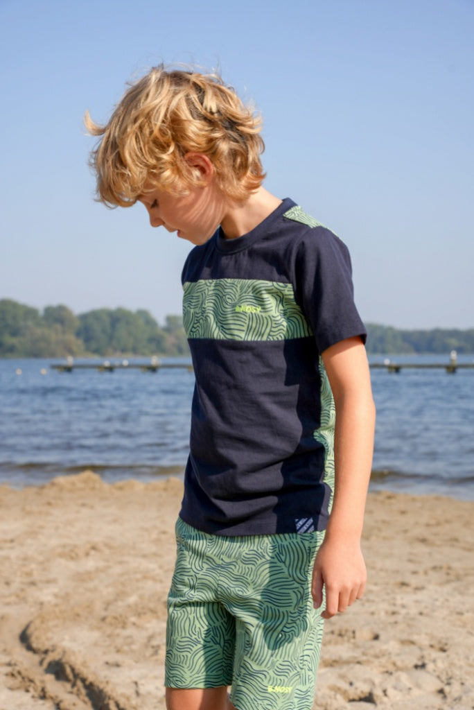 Boy wearing a navy and greenT-Shirt Tanner by B.Nosy with matching shorts on a beach.