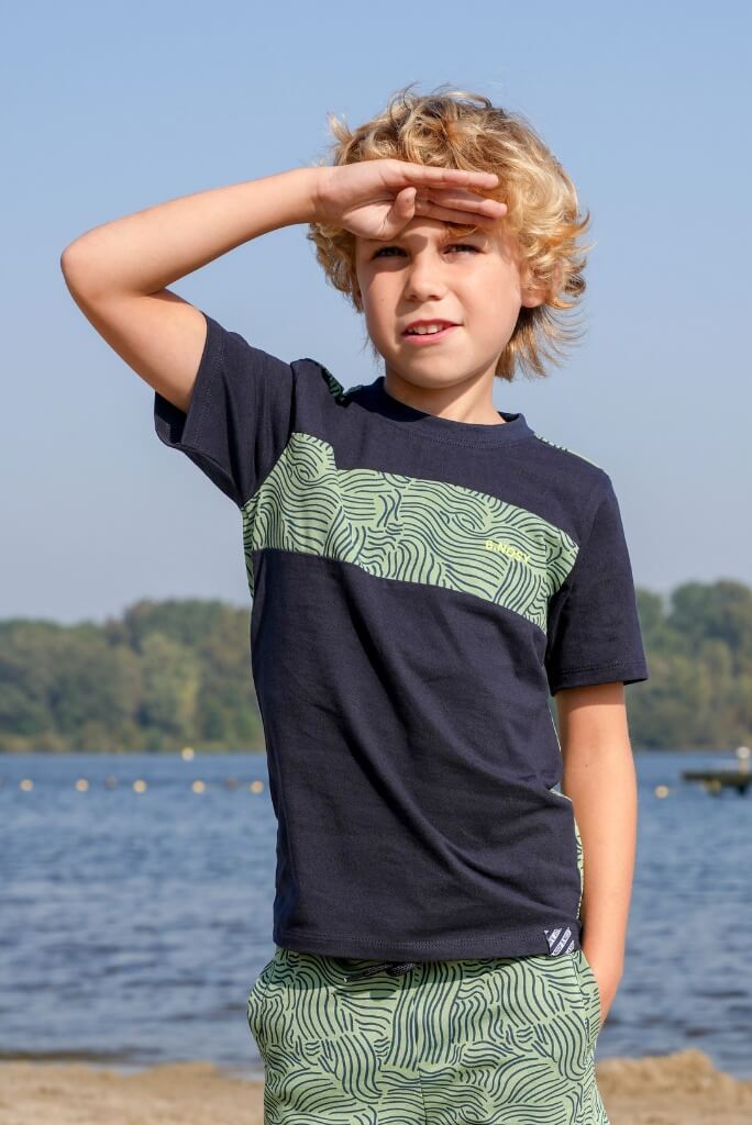 Boy wearing a navy blue and green patterned t-shirt Tanner by B.Nosy by the water.