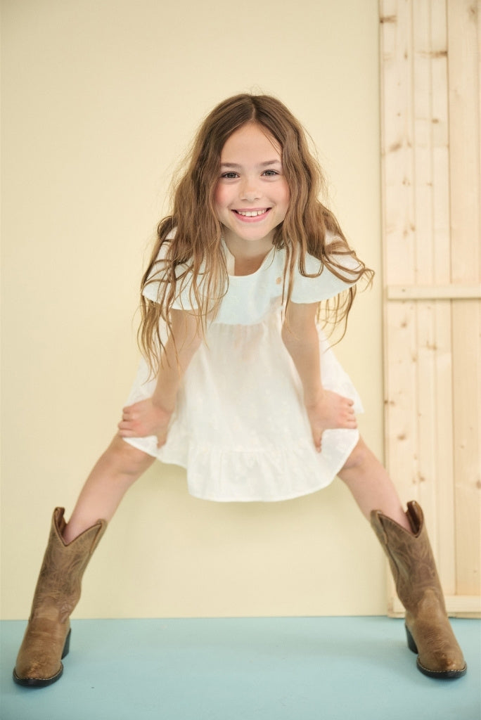 Girl looking in the camera and smiling. She's wearing the white dress Mirabel by NONO
