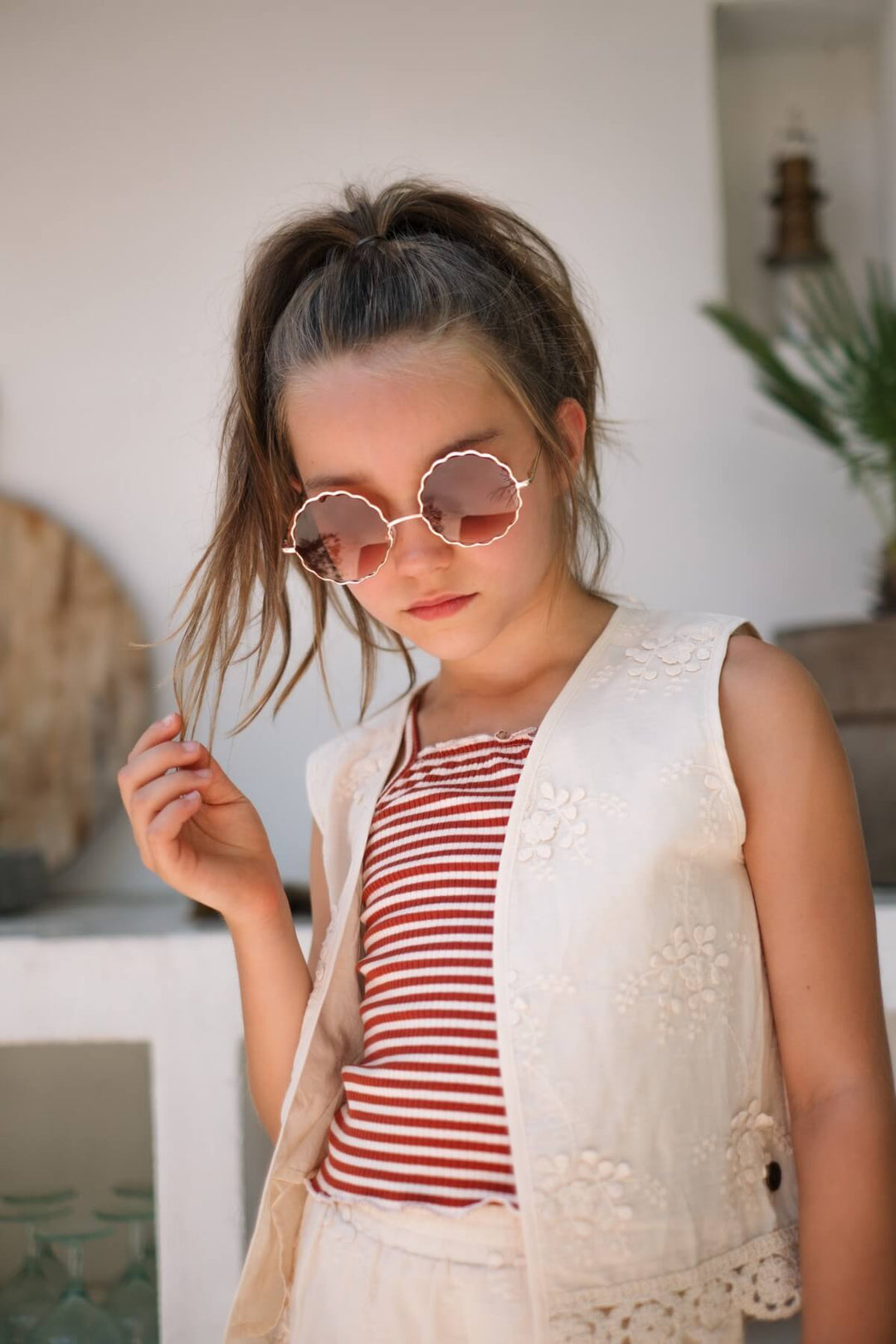 A girl wearing a striped shirt and white vest Dafne by Like FLO with pink sunglasses.