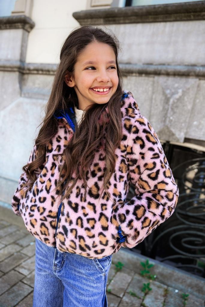 Girl wearing a pink leopard print jacket standing outdoors.