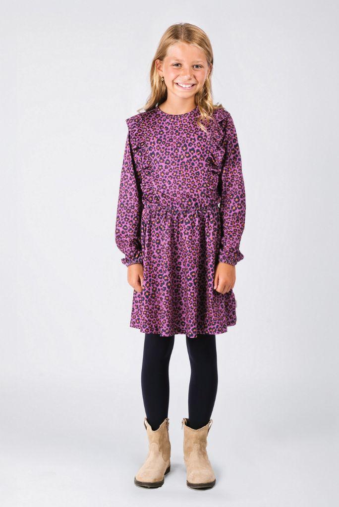 Young girl wearing a purple dress with a  floral pattern, black leggings, and beige boots on a white background