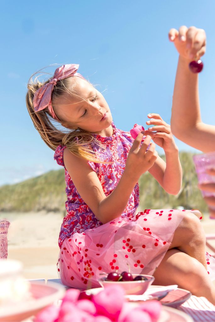 Young girl in a pink top Tamar sitting outdoors, eating cherries.