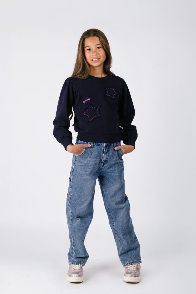 Girl wearing a dark jumper with star designs and blue jeans on a white background