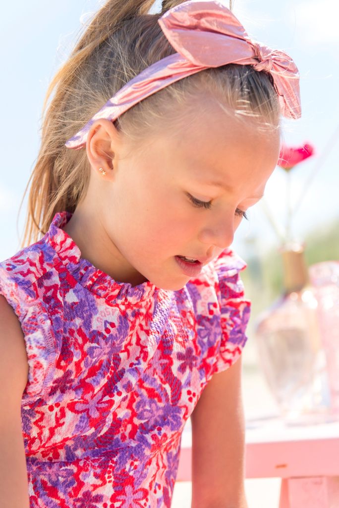Young girl wearing a colorful sleeveless top with floral patterns and a rose headband Ariane.