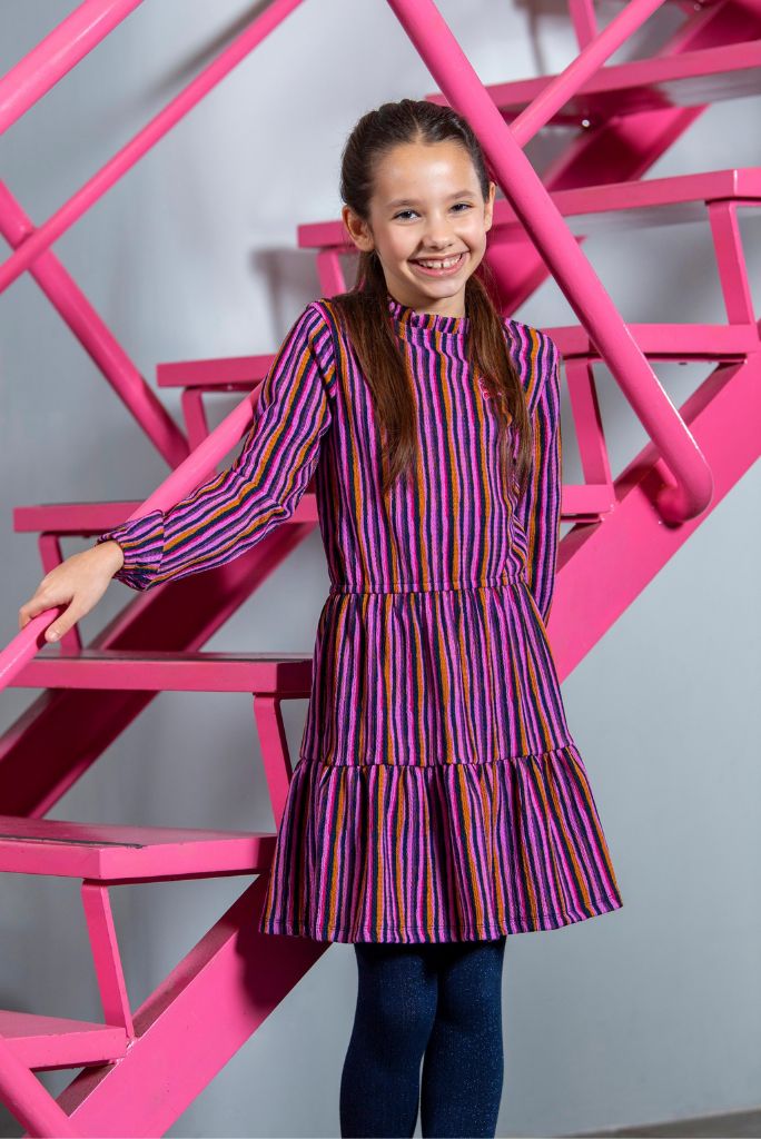 Young girl in a striped dress standing in front of a pink geometric structure.