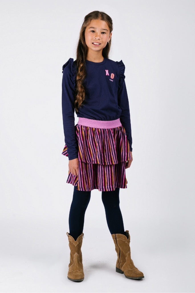 Young girl wearing a navy dress Daphne with a pink logo, striped skirt, black leggings, and brown boots on a white background.