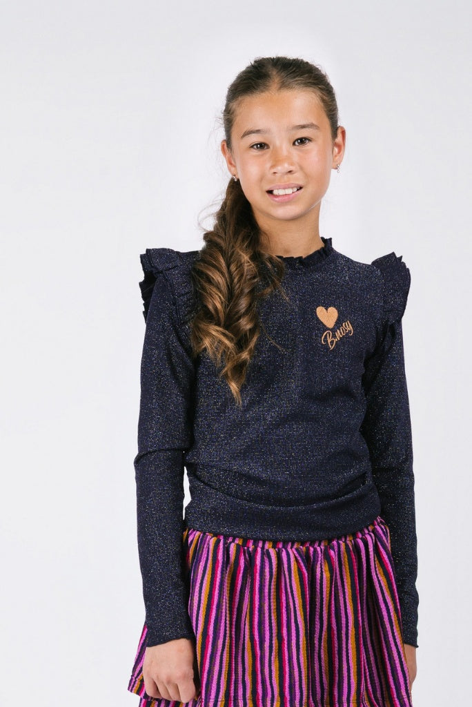 Young girl wearing a dark blue long sleeve top Tonya with a heart design and a colorful skirt on a white background