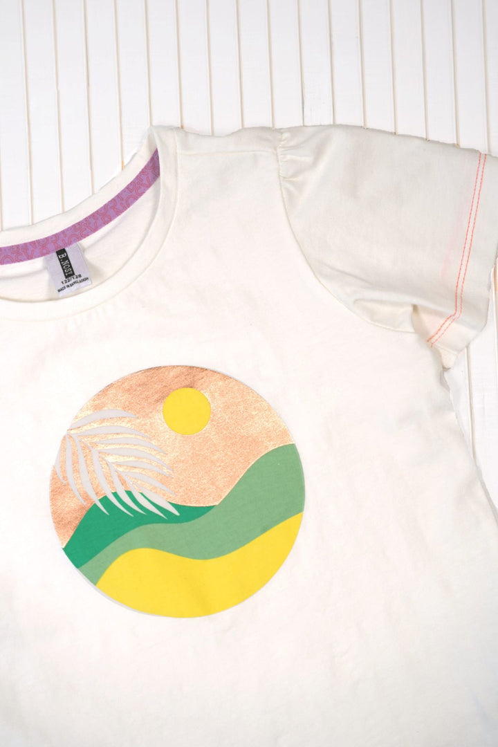 A white short-sleeve t-shirt with a circular graphic print on the front depicting a yellow sun, green hills, and a peach sky with a white palm leaf.