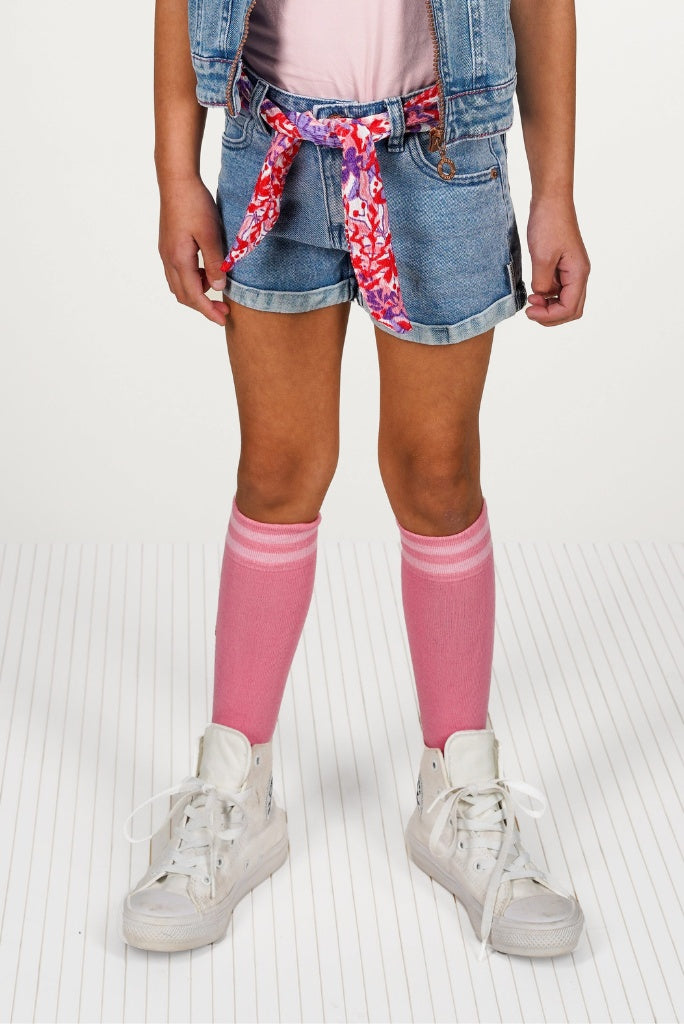 Girl wearing pink knee-high socks, denim shorts with a floral tie, and white sneakers on a light background