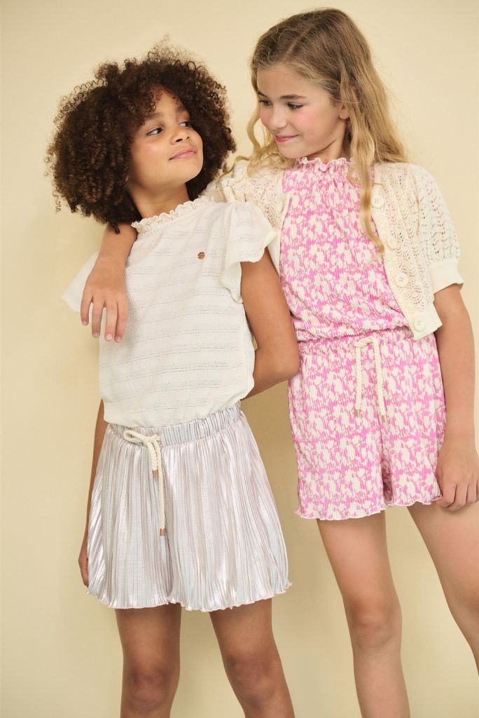 Two young girls wearing playsuits against a beige background