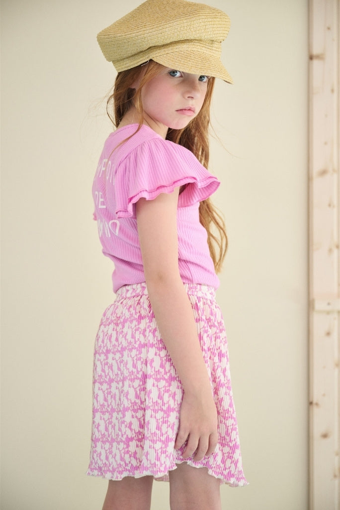 Girl wearing a hat an standing with the back. She's wearing the pleated purple dress Morly by NONO.