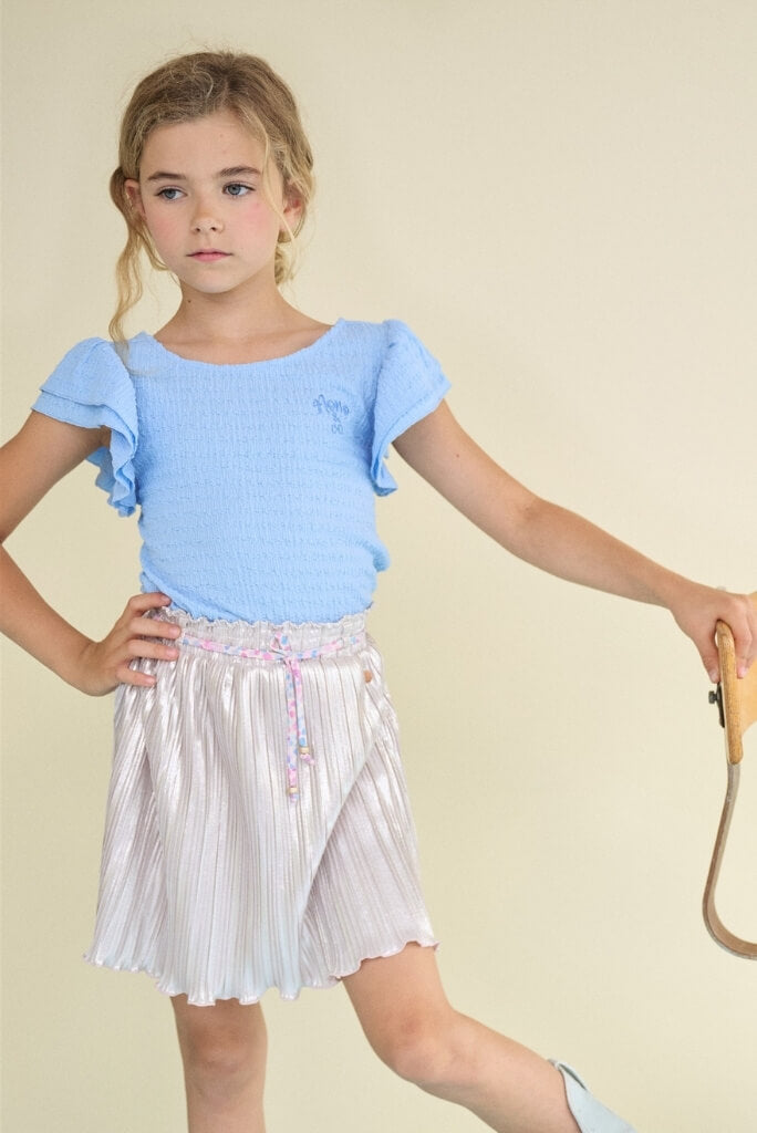 Girl looking to the side and wearing the silver pleated skirt Norah by NONO.
