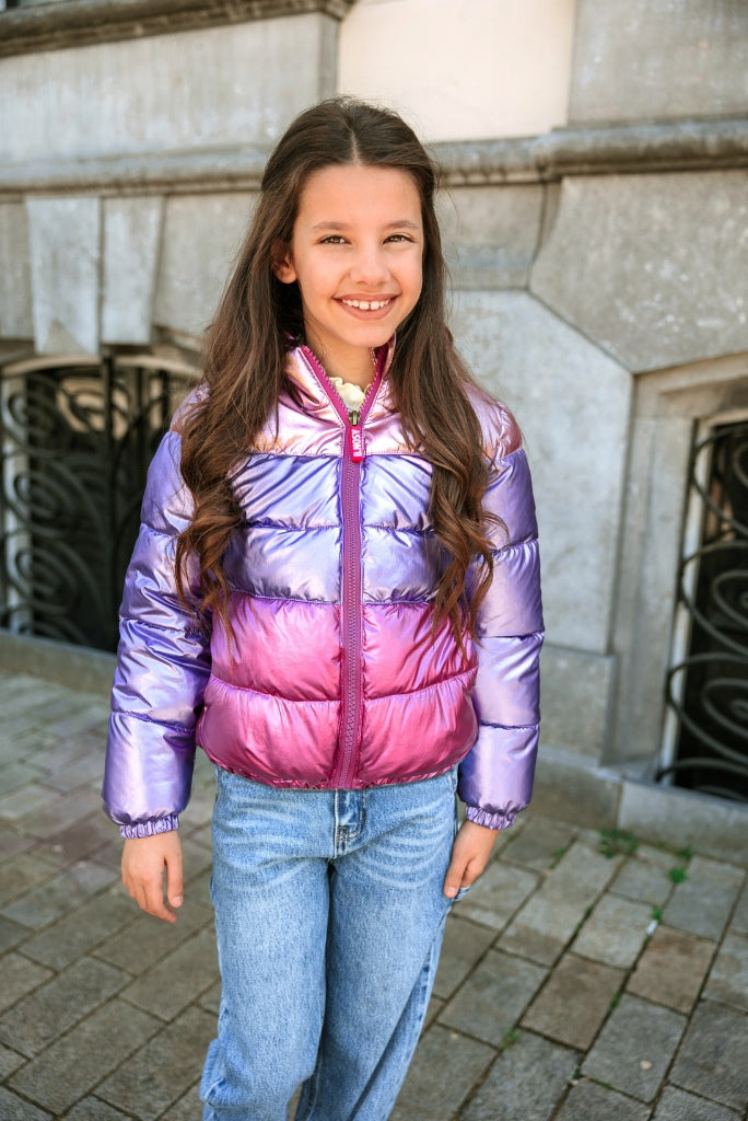 Young girl wearing a colorful puffer jacket standing outdoors.