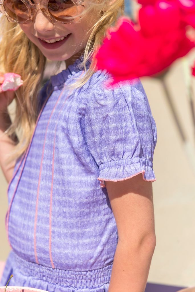 Girl wearing the purple dress Dotty with pink accents outdoors