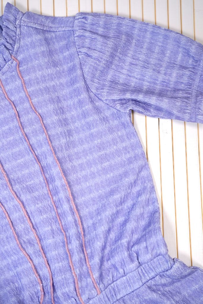 Close-up of the purple dress Dotty with pink stitching on a wooden surface