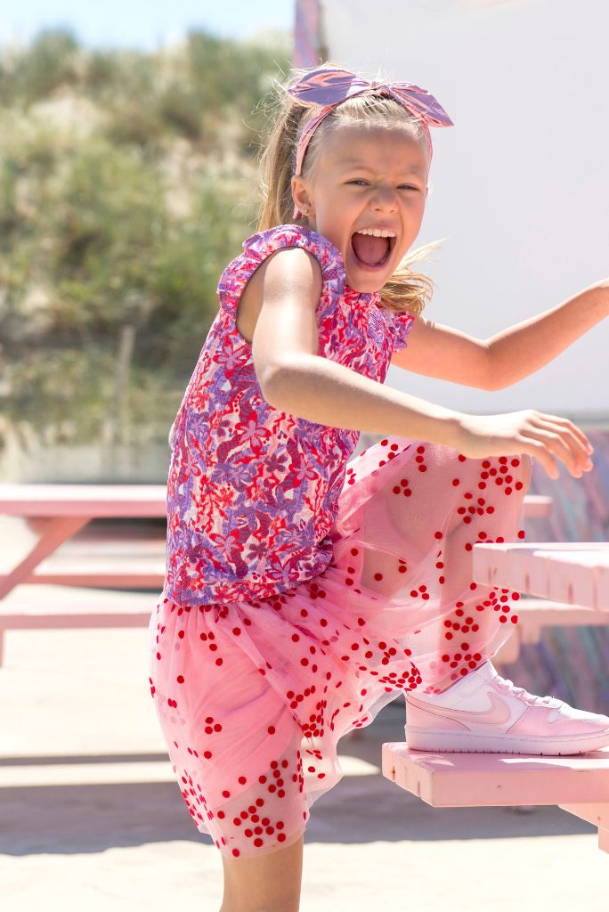 Young girl in a pink tulle skirt River with red polka dots, standing outdoors.