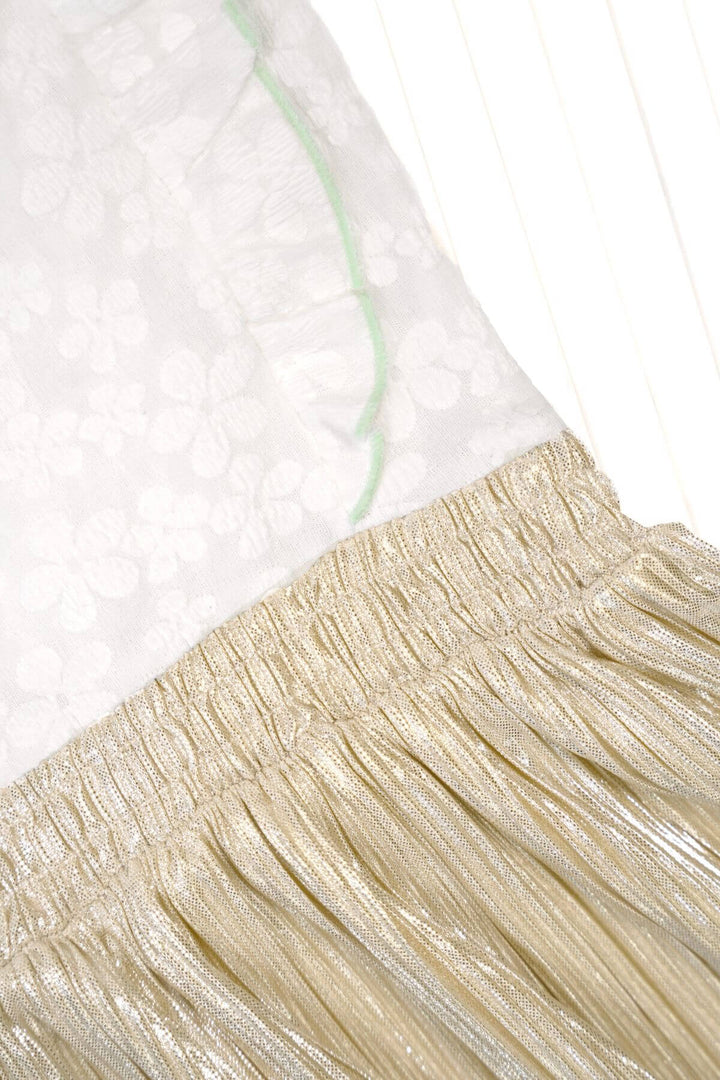 Close-up detail of a dress showing a white sheer floral top part with a thin mint green stitch line and a pleated metallic champagne-gold fabric section below it.