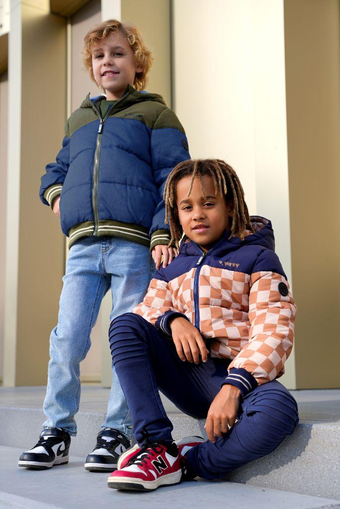 Two children wearing colorful jackets standing on a sidewalk.