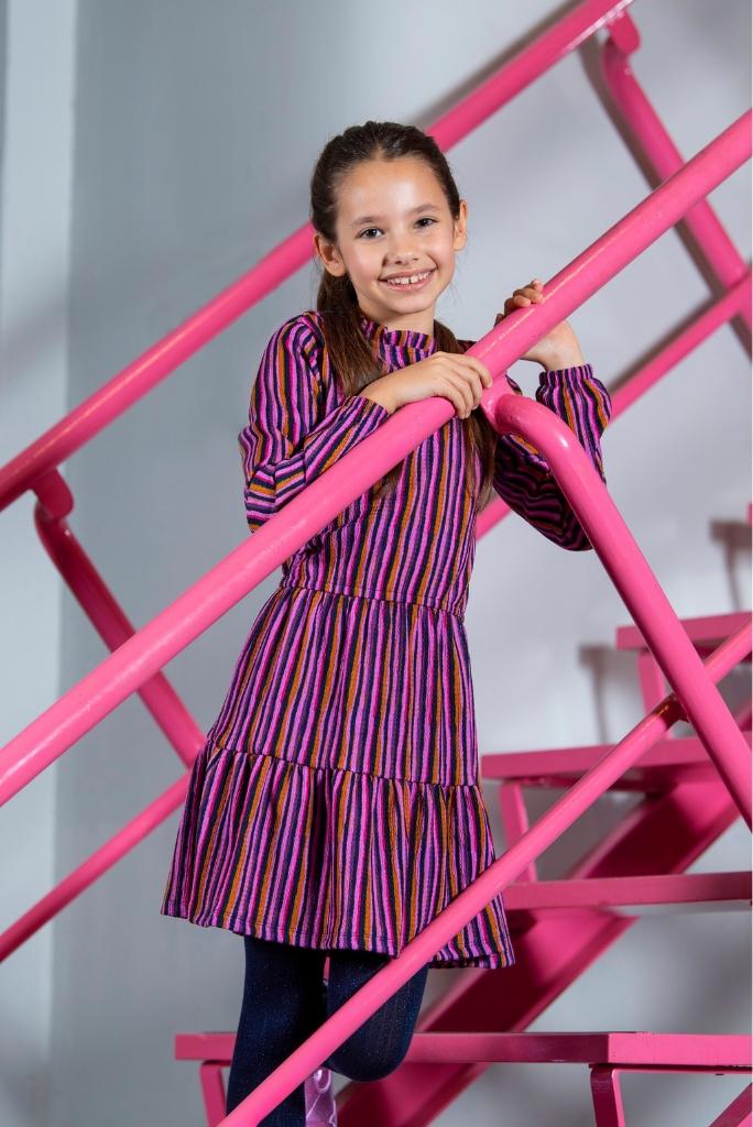 Young girl in a colorful dress standing on a pink metal staircase.