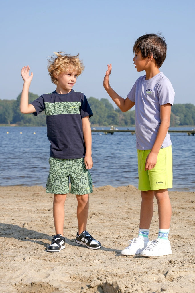 Two children on a beach giving high fives with a body of water and trees in the background.