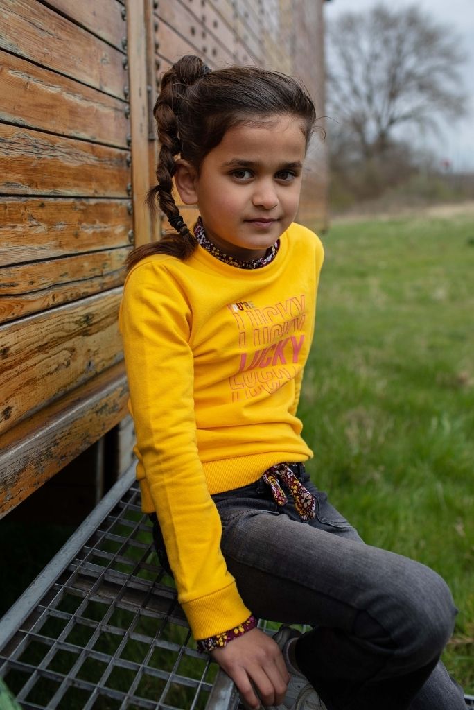 Girl wearing the yellow jumper Kato by Quapi and sitting down